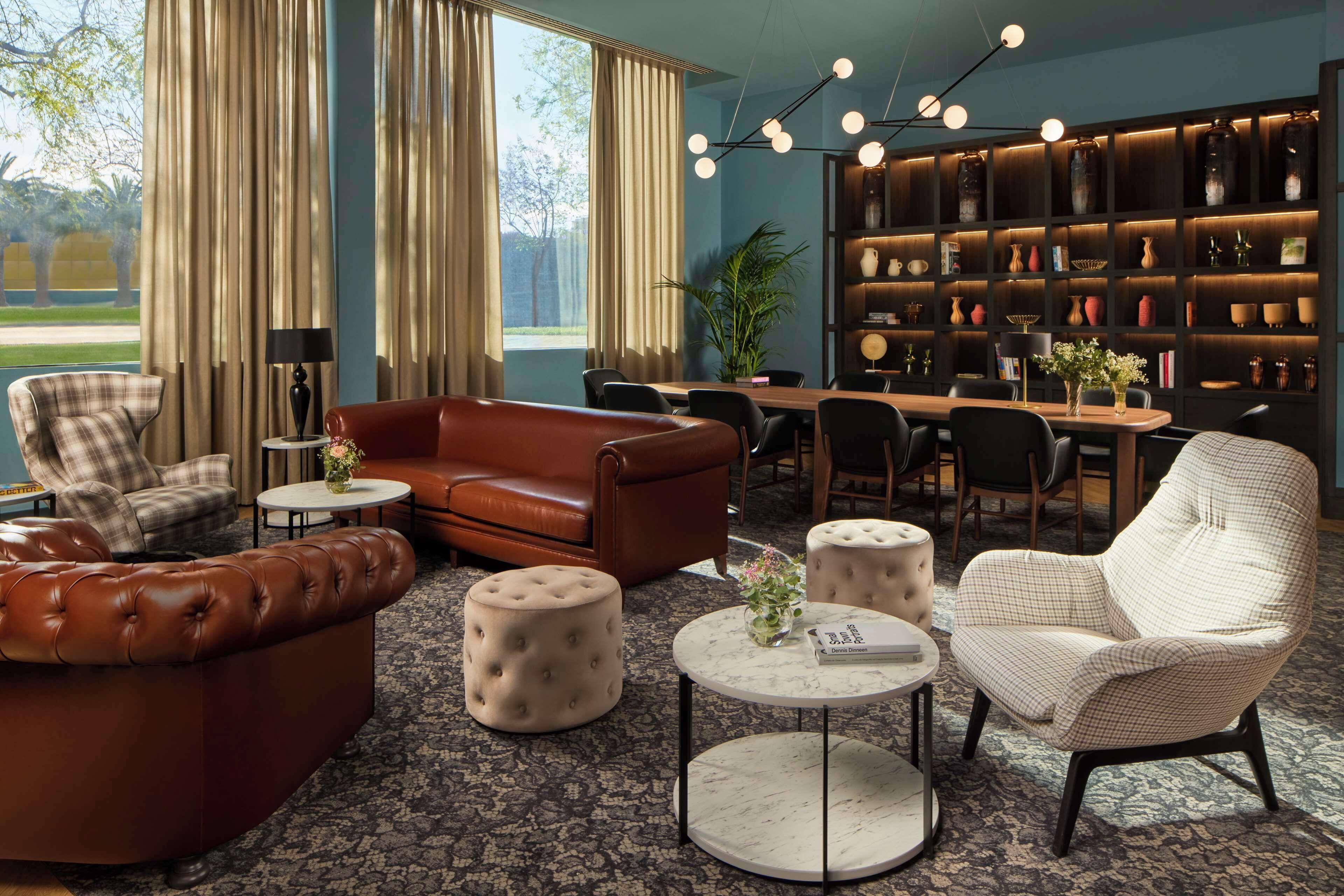A modern living room with a brown leather sofa, a white armchair, and a dining area with a wooden table and chairs. There is a bookshelf filled with decorative items and a large window with curtains.