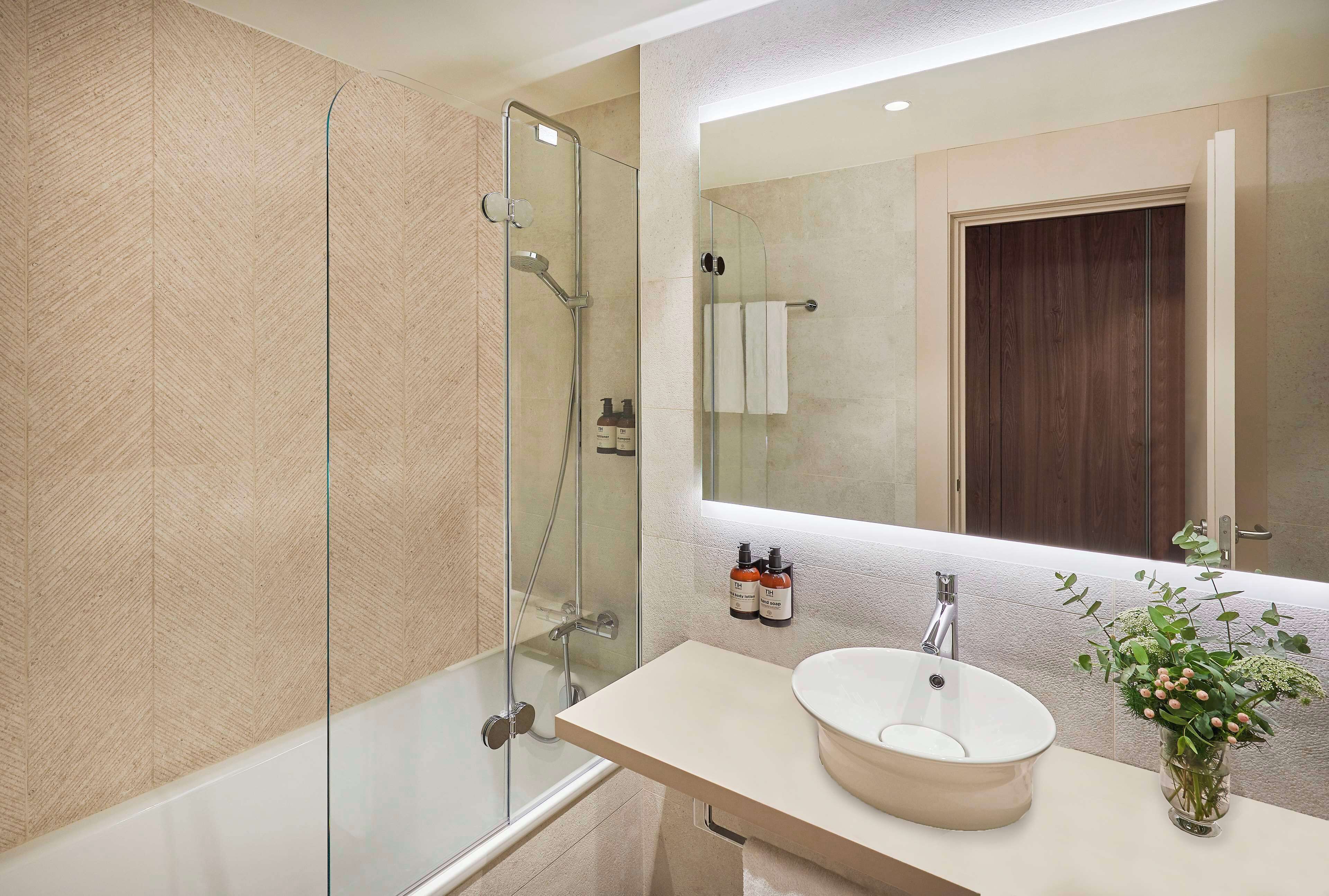 A modern bathroom with a glass shower enclosure, a white sink with a round basin, and a mirror above the sink.