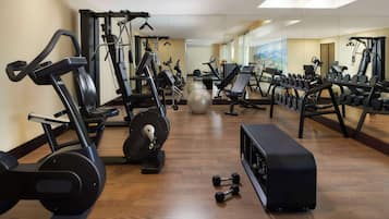 Un gimnasio con diverso equipo de ejercicio, incluyendo cintas de correr, máquinas de pesas y mancuernas.