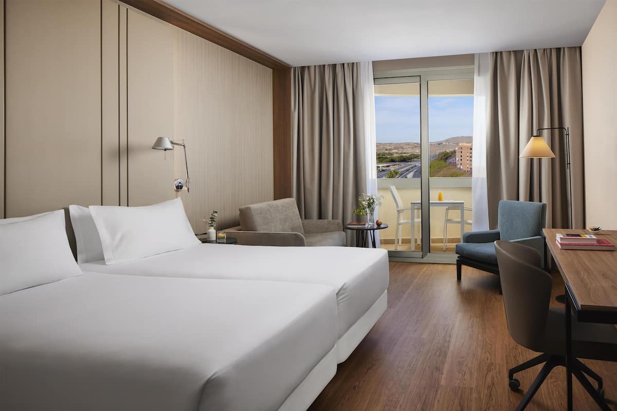 Ein Hotelzimmer mit einem großen Bett, einem Schreibtisch, einem Stuhl und Blick auf die Stadt.