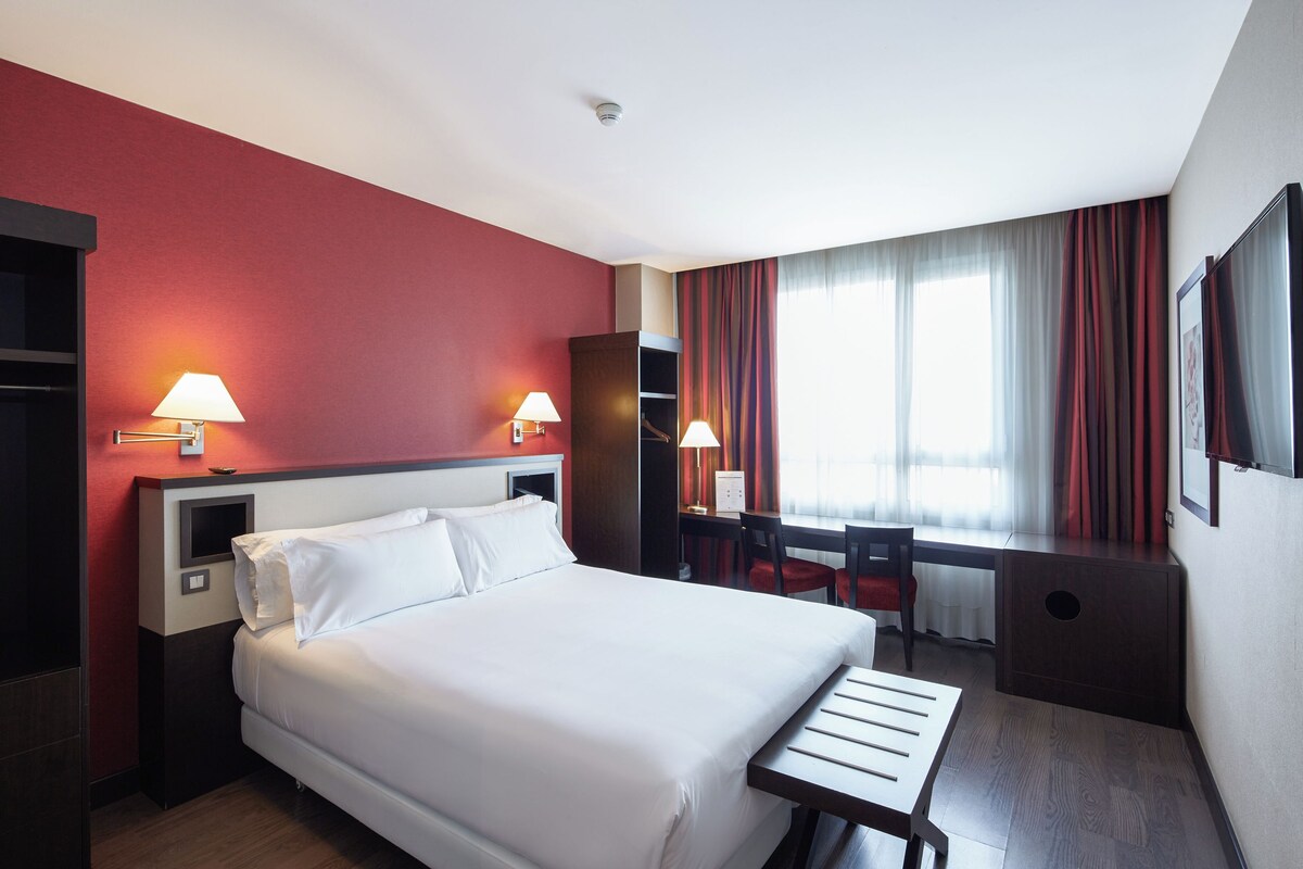 Habitación de hotel con una cama grande, dos lámparas de noche, un escritorio con silla y un televisor en la pared.