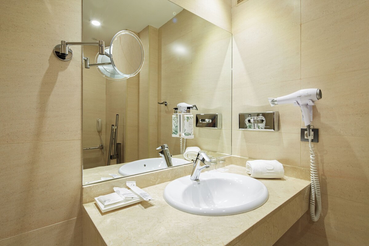 Un baño moderno con un espejo grande, un lavabo, un secador de pelo y un perchero para toallas.