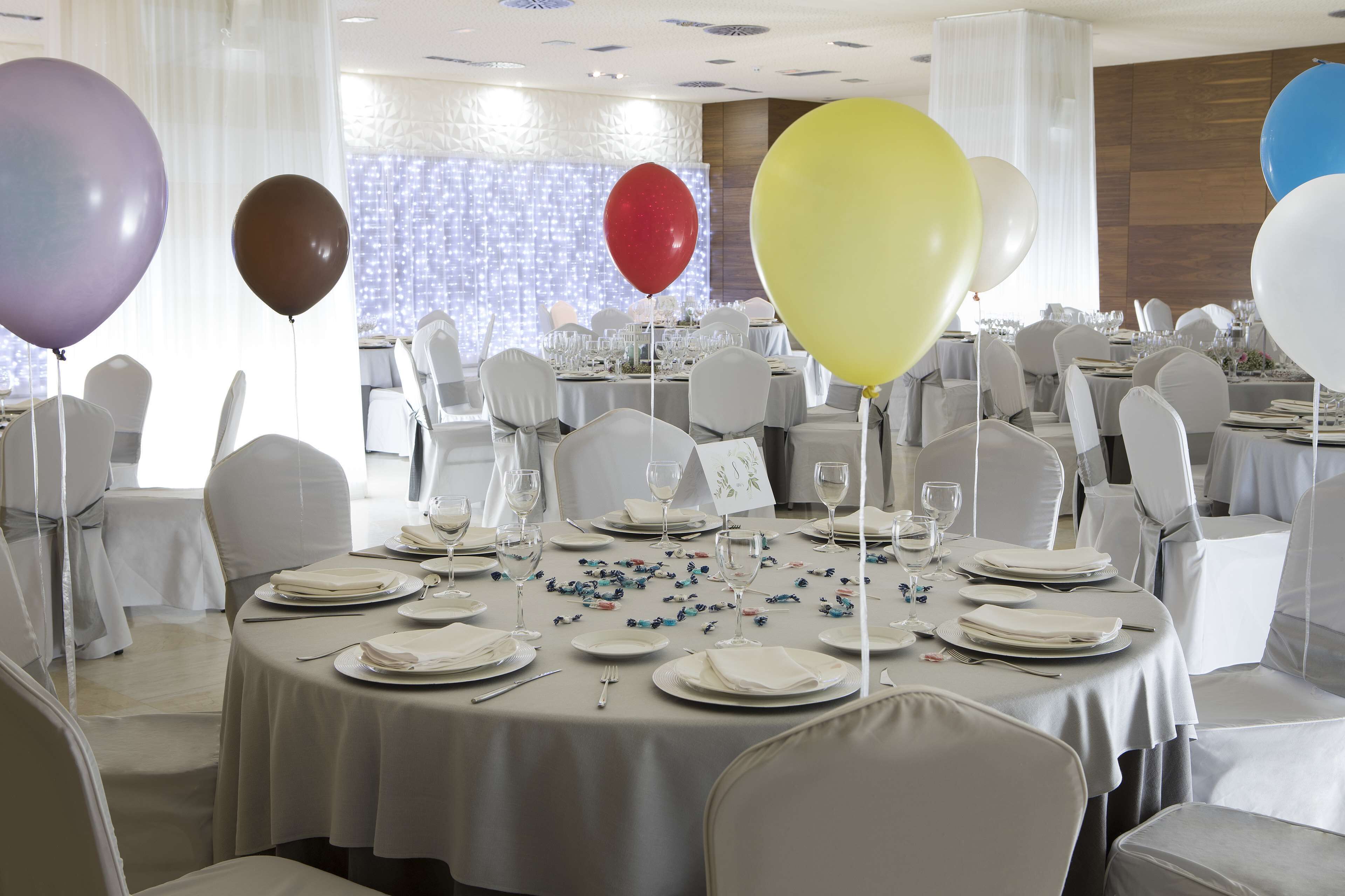 Un salón de banquetes con mesas redondas dispuestas para un evento formal, con manteles blancos, sillas y un centro de mesa floral.