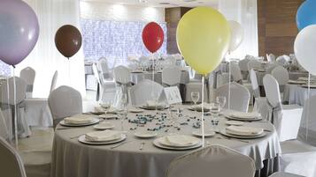 Un salón de banquetes con mesas redondas dispuestas para un evento formal, con manteles blancos, sillas y un centro de mesa floral.