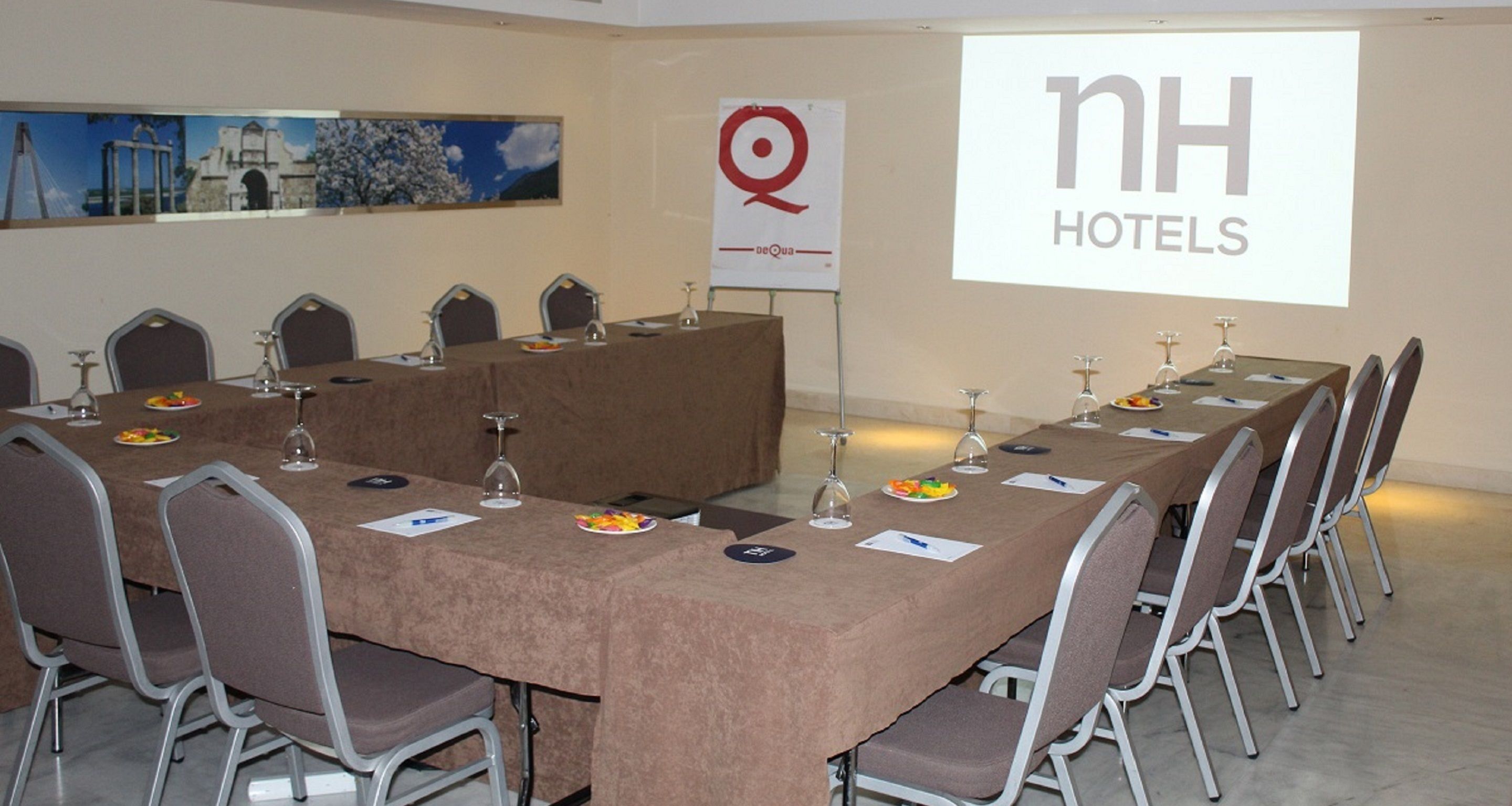 Un salón de conferencias con una larga mesa, sillas y una pantalla de proyector que muestra 'NH HOTELS'.