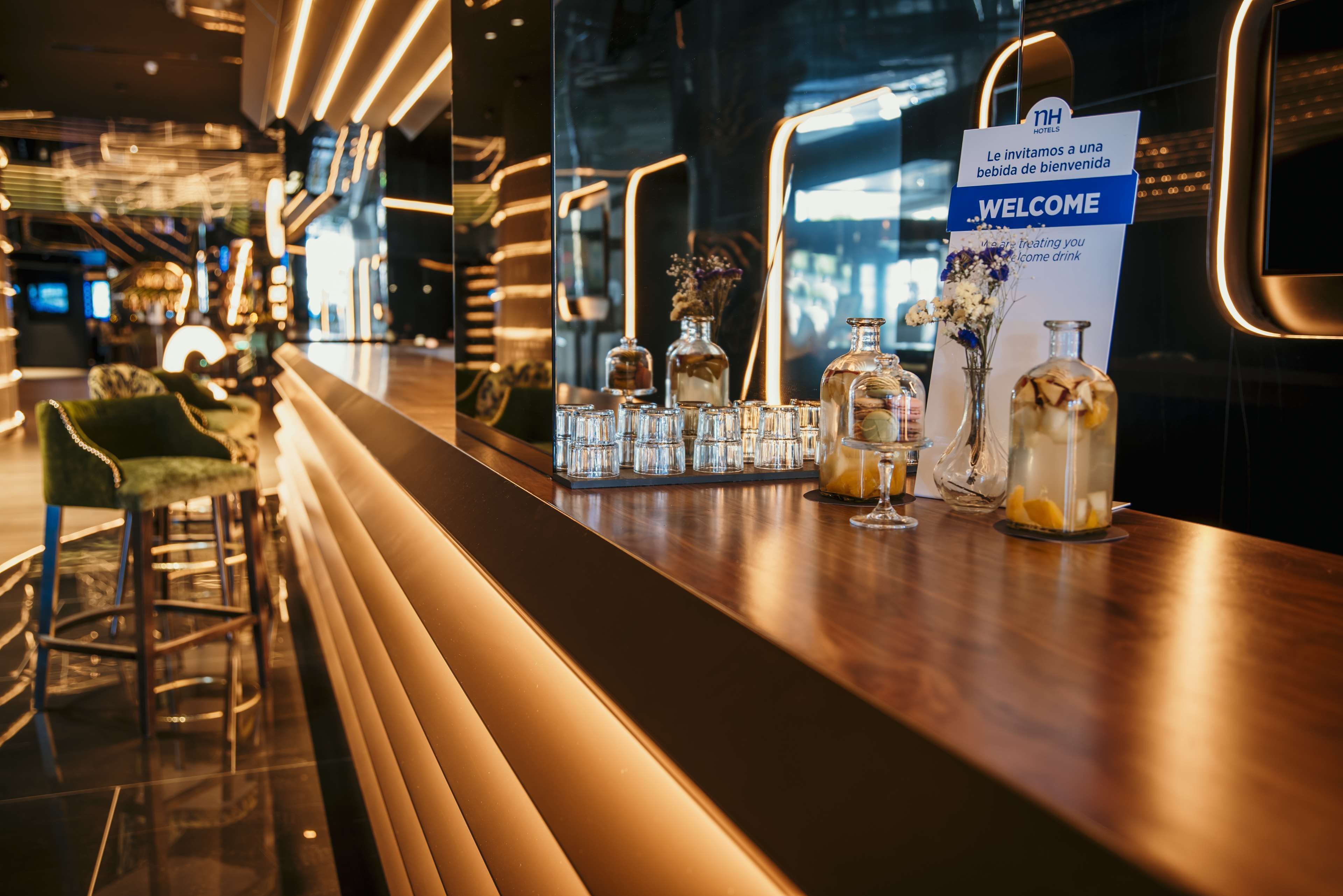 A bar area with a 'WELCOME' sign, bar stools, and various bottles and glasses on the counter.