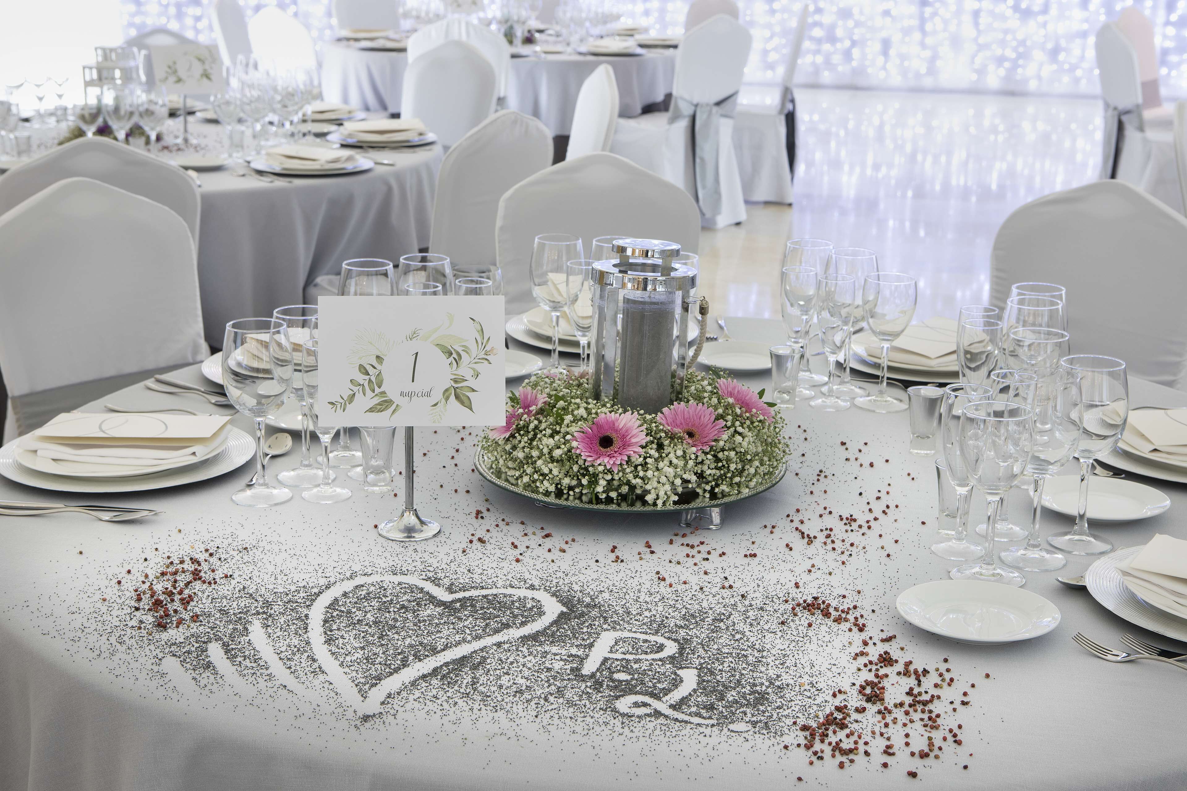 A wedding reception table set with white tablecloths, silverware, and wine glasses.