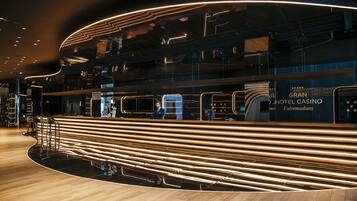 A modern hotel lobby with a curved reception desk, multiple seating areas, and a visible staircase.
