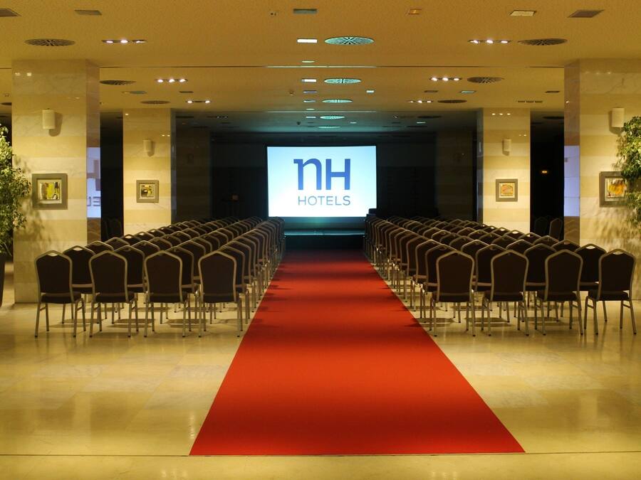 Un vestíbulo de hotel con una alfombra roja que conduce a una zona de estar con filas de sillas.