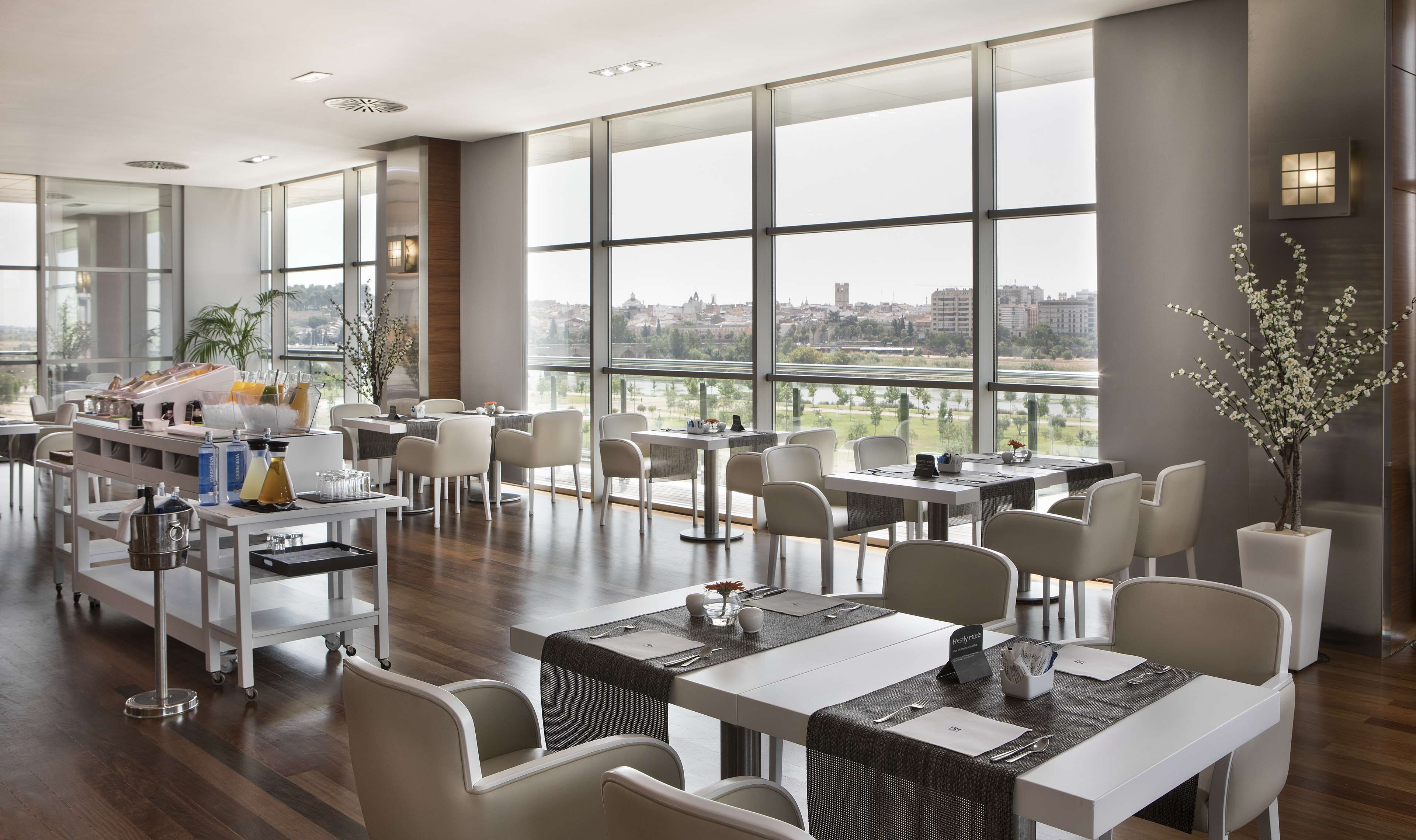 Un comedor moderno con ventanas amplias, mobiliario blanco y vistas a la ciudad.