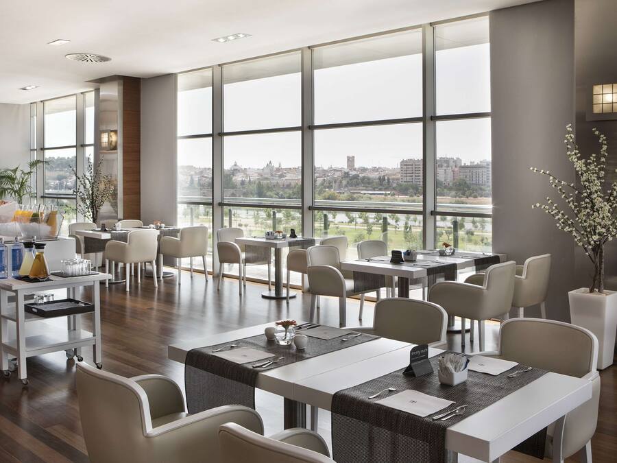 Un comedor moderno con ventanas amplias, mobiliario blanco y vistas a la ciudad.