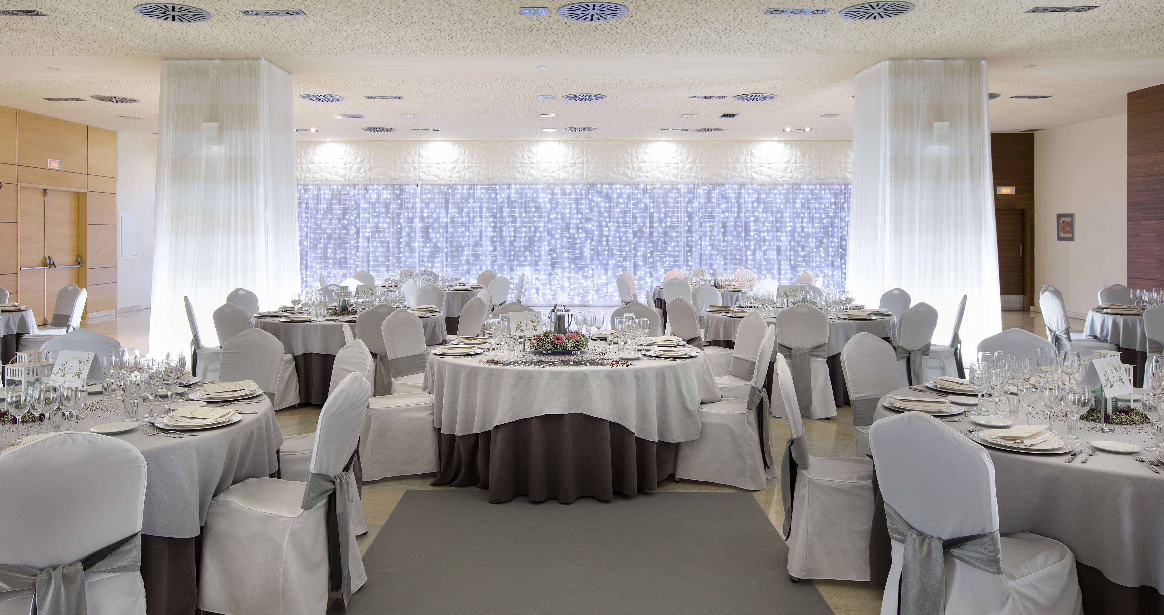 A banquet hall with round tables, white tablecloths, and chairs with grey sashes.