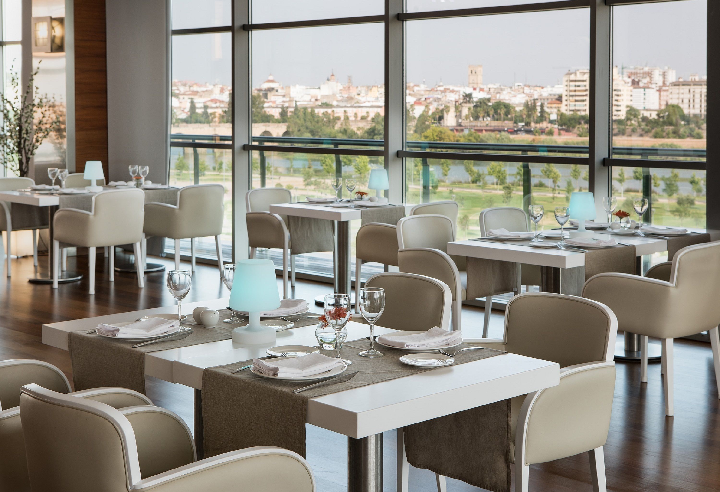 Un restaurante con mesas dispuestas para comer, amplios ventanales que ofrecen vistas de la ciudad.