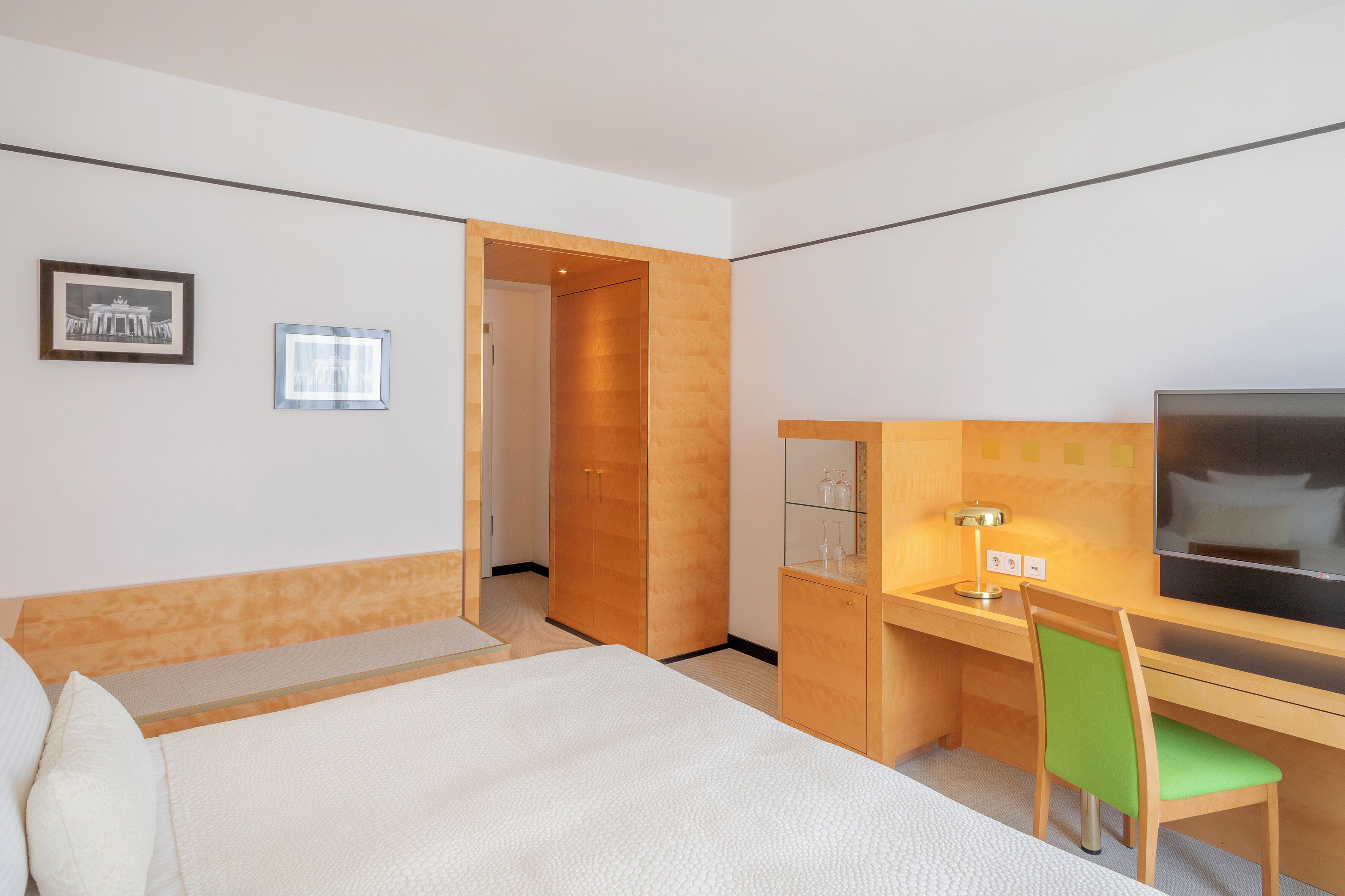 Una habitación de hotel con una cama, un escritorio con silla, un televisor y una puerta que da a otra habitación.