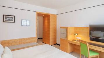 Una habitación de hotel con una cama, un escritorio con silla, un televisor y una puerta que da a otra habitación.