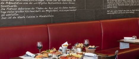 A restaurant interior with a red booth seating area, a table set with various dishes, wine glasses, and a chalkboard menu.