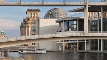 Un puente moderno con un barco pasando por debajo, un edificio histórico y una estructura de vidrio contemporánea.