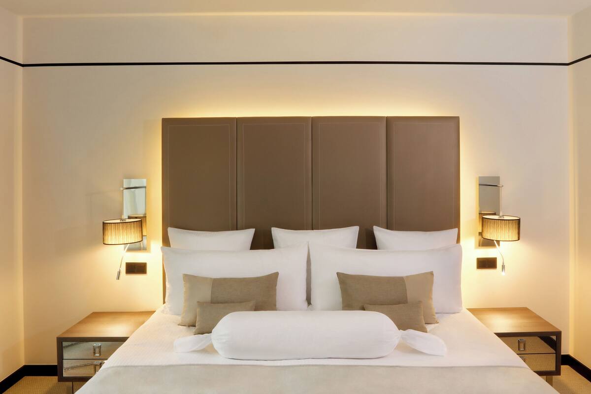 A modern hotel room with a large bed, two bedside tables, and wall-mounted lamps.