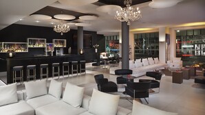 A modern lounge area with a bar, white sofas, black chairs, and a chandelier. - Melia Berlin (Berlin)