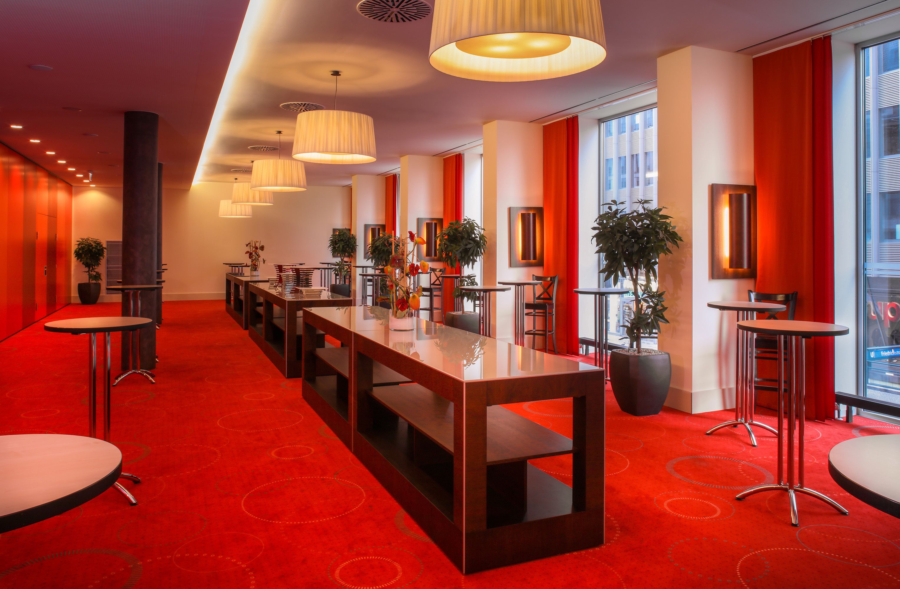 A hotel lobby with a long reception desk, multiple seating areas, and large windows.
