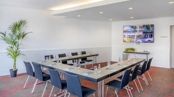 A conference room with a long table, chairs, a potted plant, and a TV screen displaying 'MELIA BERLIN'.