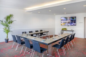 A conference room with a long table, chairs, a potted plant, and a TV screen displaying 'MELIA BERLIN'.