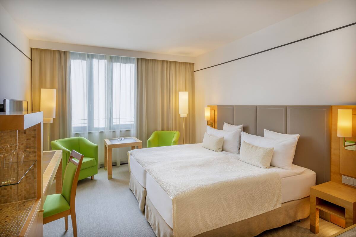 A hotel room with a large bed, a desk with a chair, a small table, and a TV.