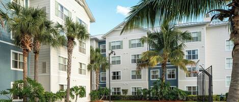 A courtyard with a basketball court, palm trees, and a building with multiple windows and balconies.