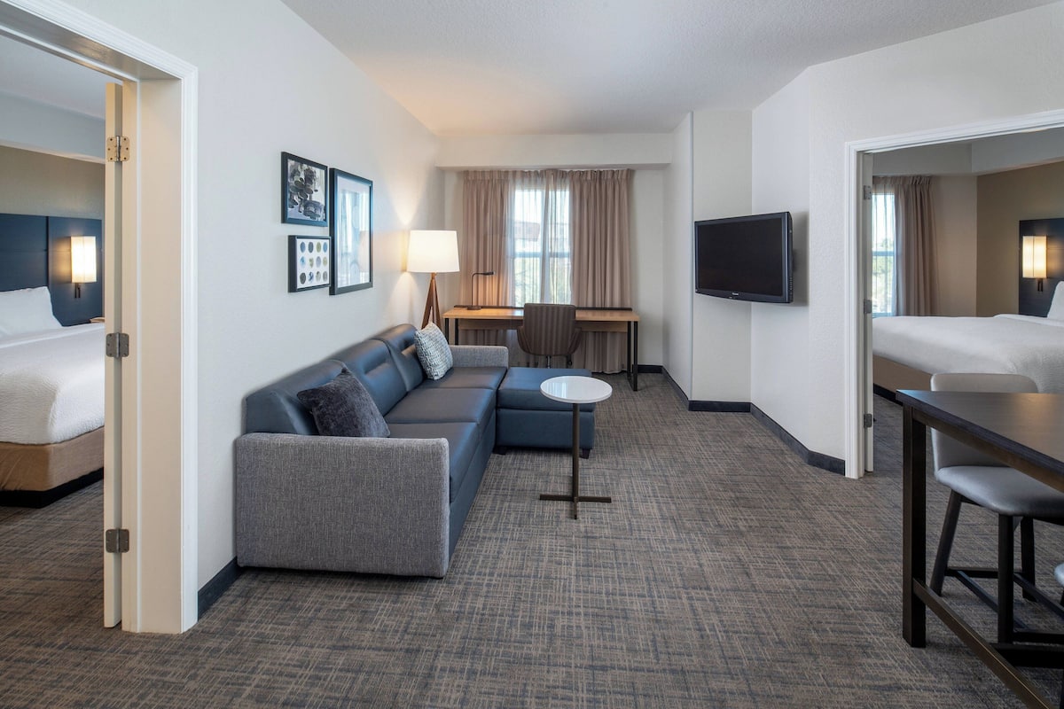 A hotel room with a bed, a sofa, a desk, a TV, and a small table.