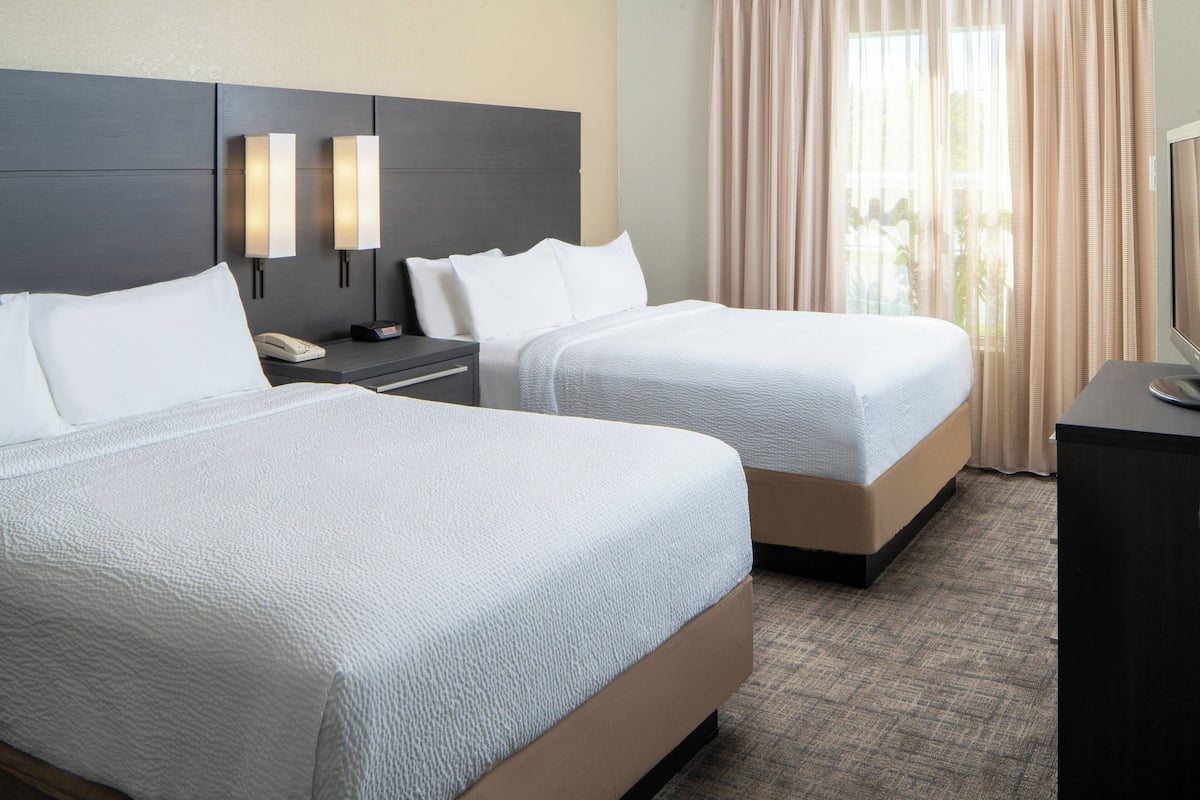 A hotel room with two beds, a nightstand with a phone, and a desk with a computer.