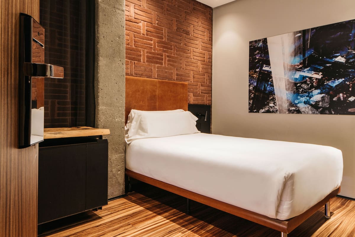 Une chambre moderne avec un lit en bois, un mur décoratif en briques et une œuvre d’art accrochée au mur.