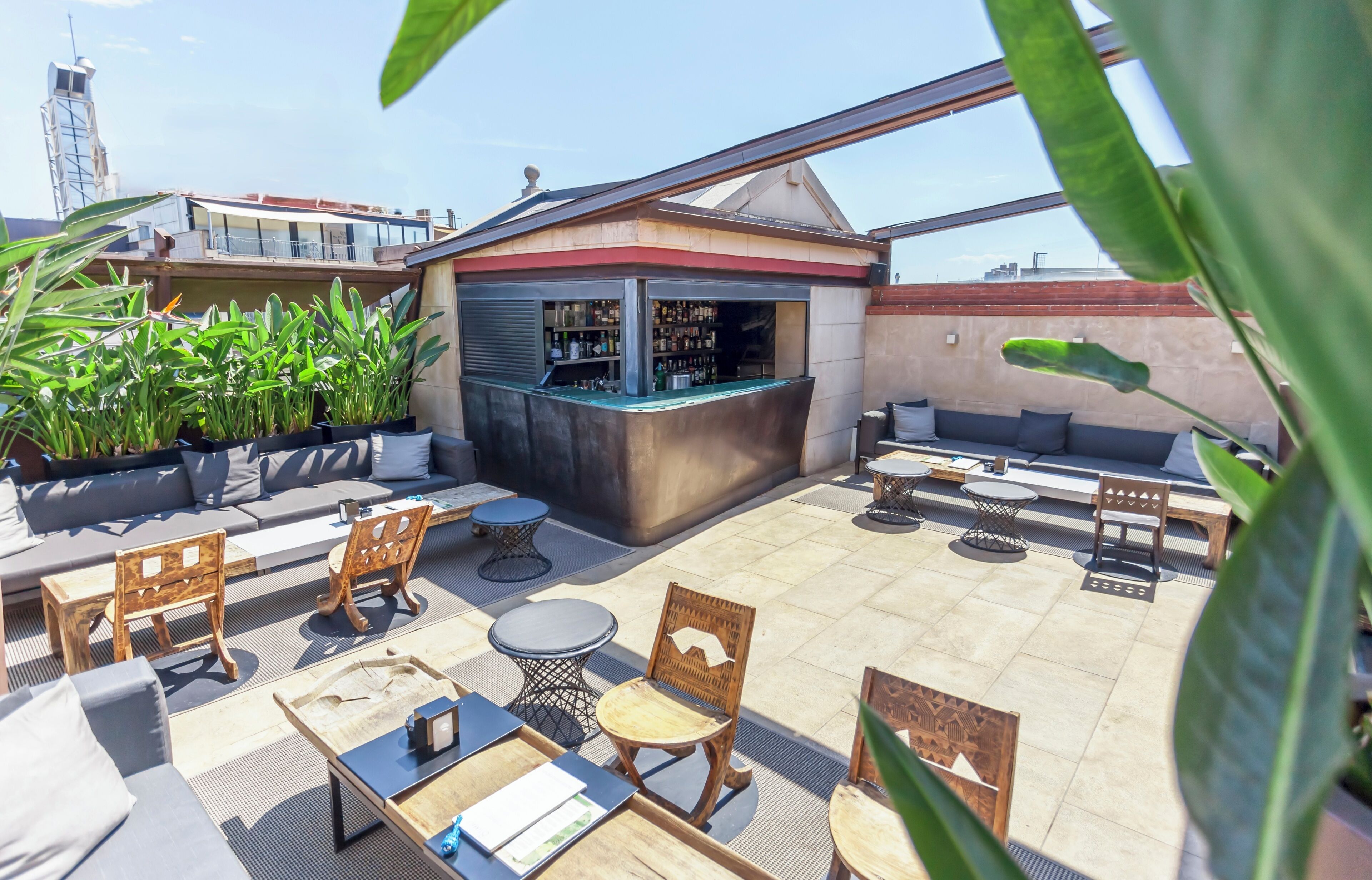 A rooftop bar with seating, a bar counter, and potted plants.