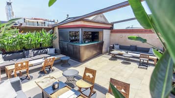 A rooftop bar with seating, a bar counter, and potted plants.