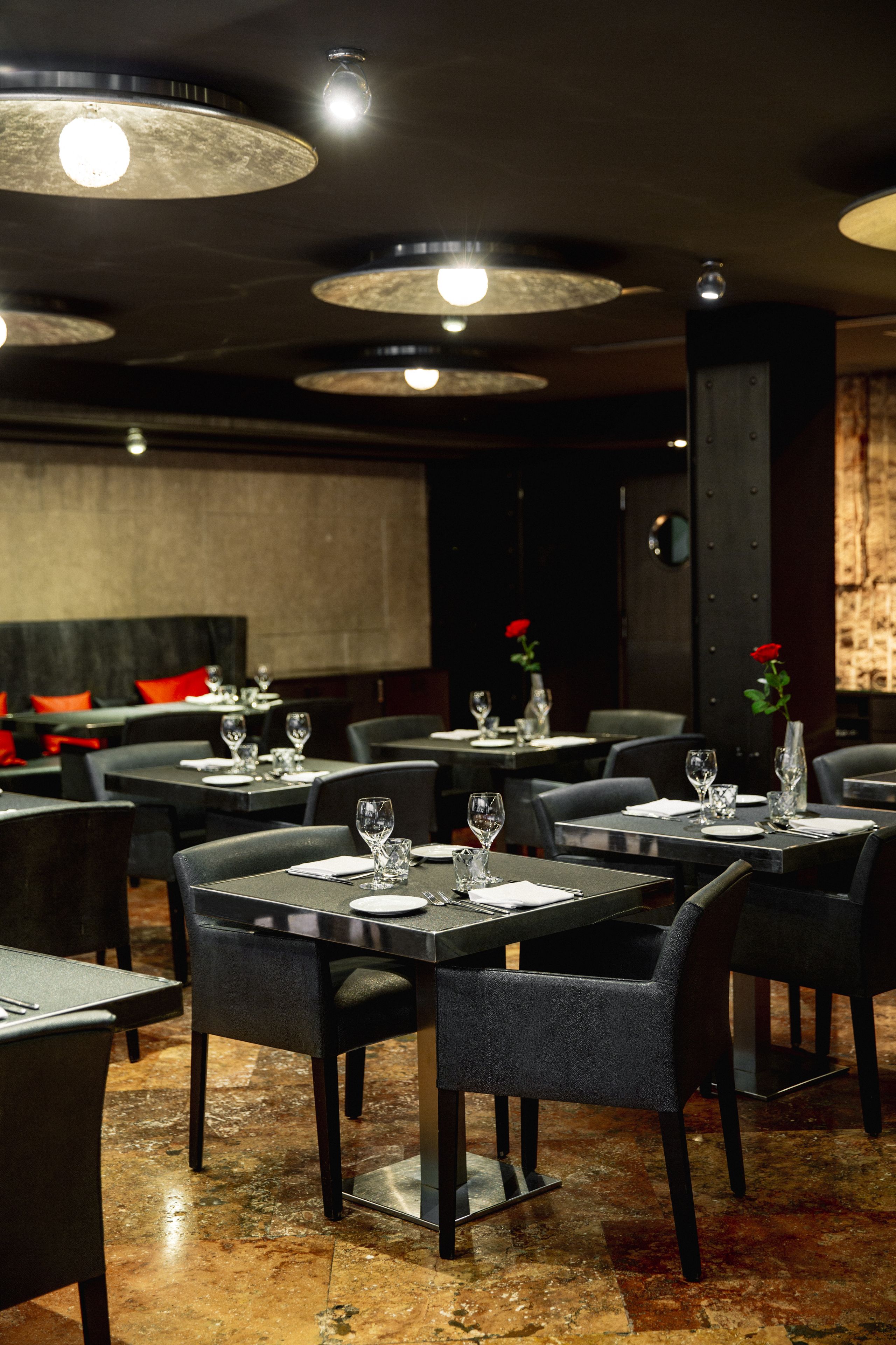 A restaurant with round tables, black chairs, and a brick wall in the background.