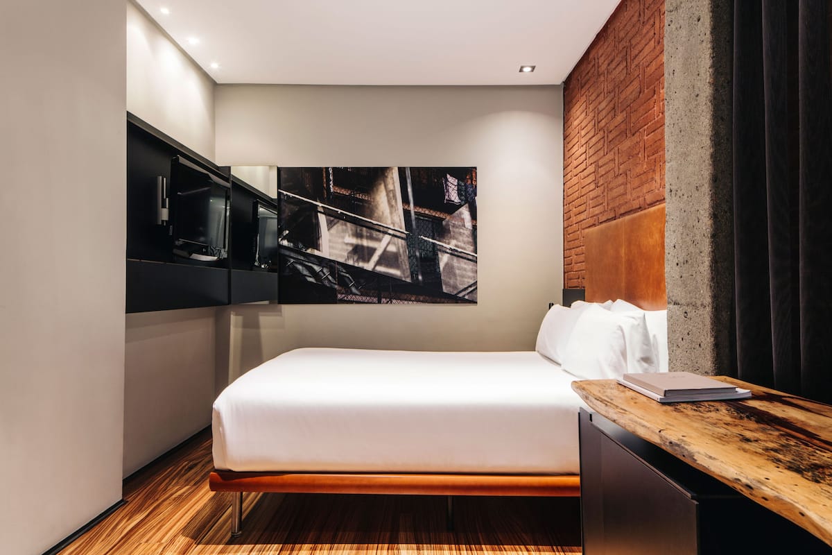Une chambre d’hôtel moderne avec un lit, un bureau en bois, un grand tableau abstrait et un mur décoratif en briques.