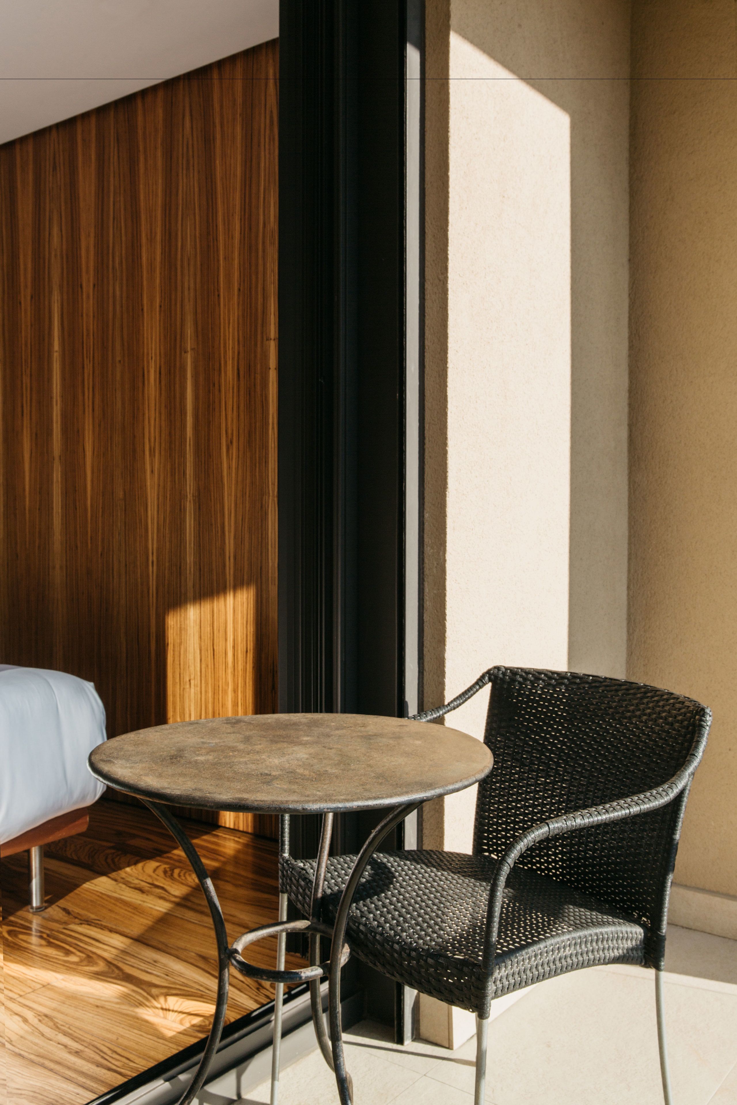 Una habitación pequeña con una cama, una mesa redonda y una silla de mimbre.