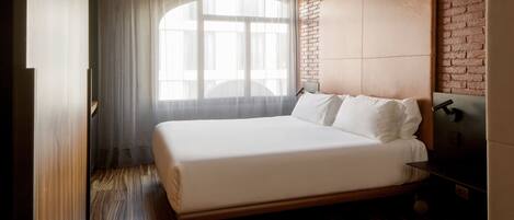 Una habitación de hotel moderna con una cama grande, una pared decorativa de ladrillo y un ventanal con cortinas translúcidas.