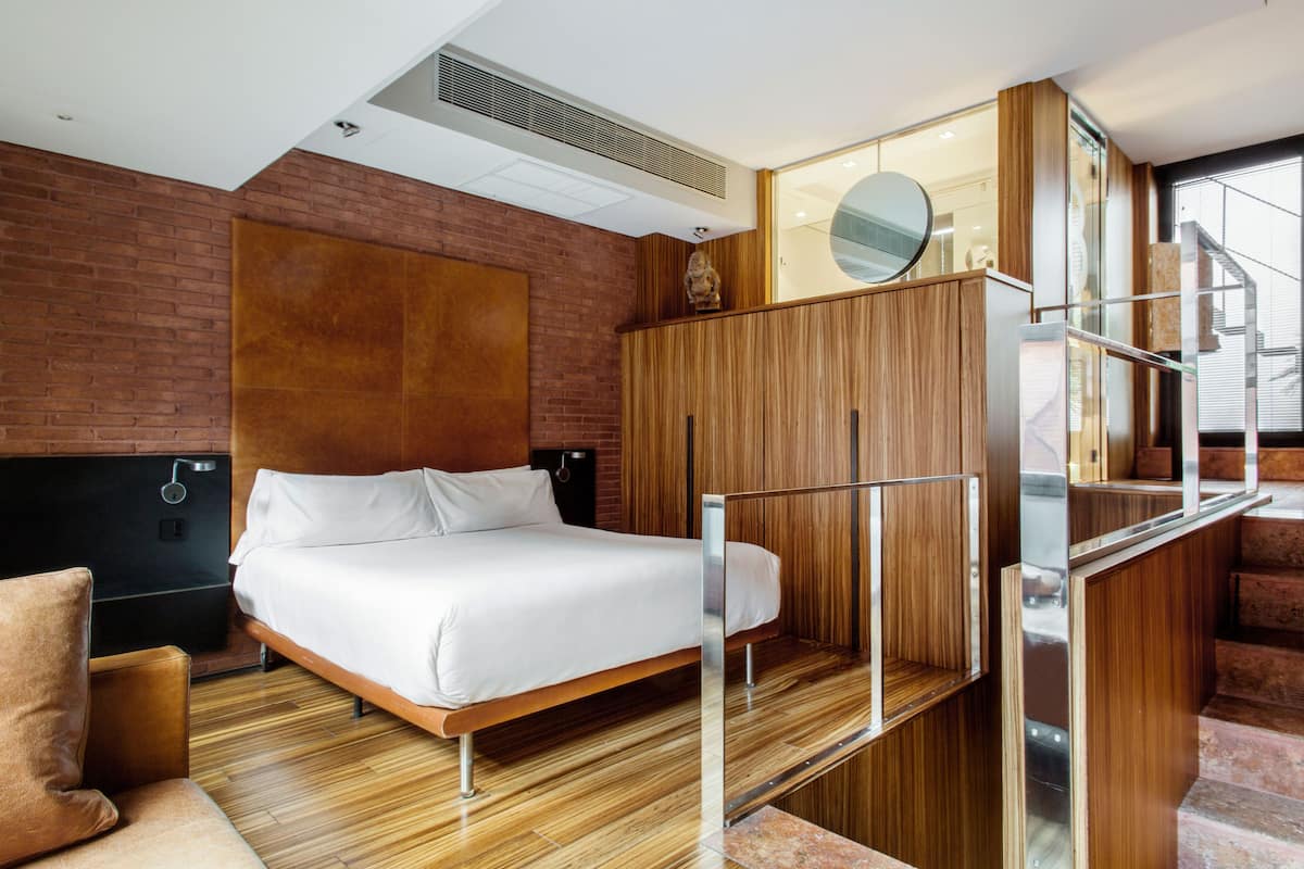 Une chambre d’hôtel moderne avec un lit en bois, un mur décoratif en briques, une armoire en bois et un escalier.