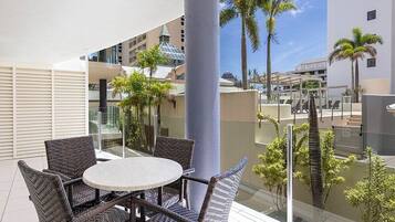 A balcony with wicker furniture, a glass railing, and palm trees.