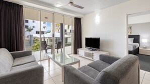 Una habitación de hotel moderna con balcón, televisor de pantalla plana, sofás grises y una mesa de centro de vidrio.