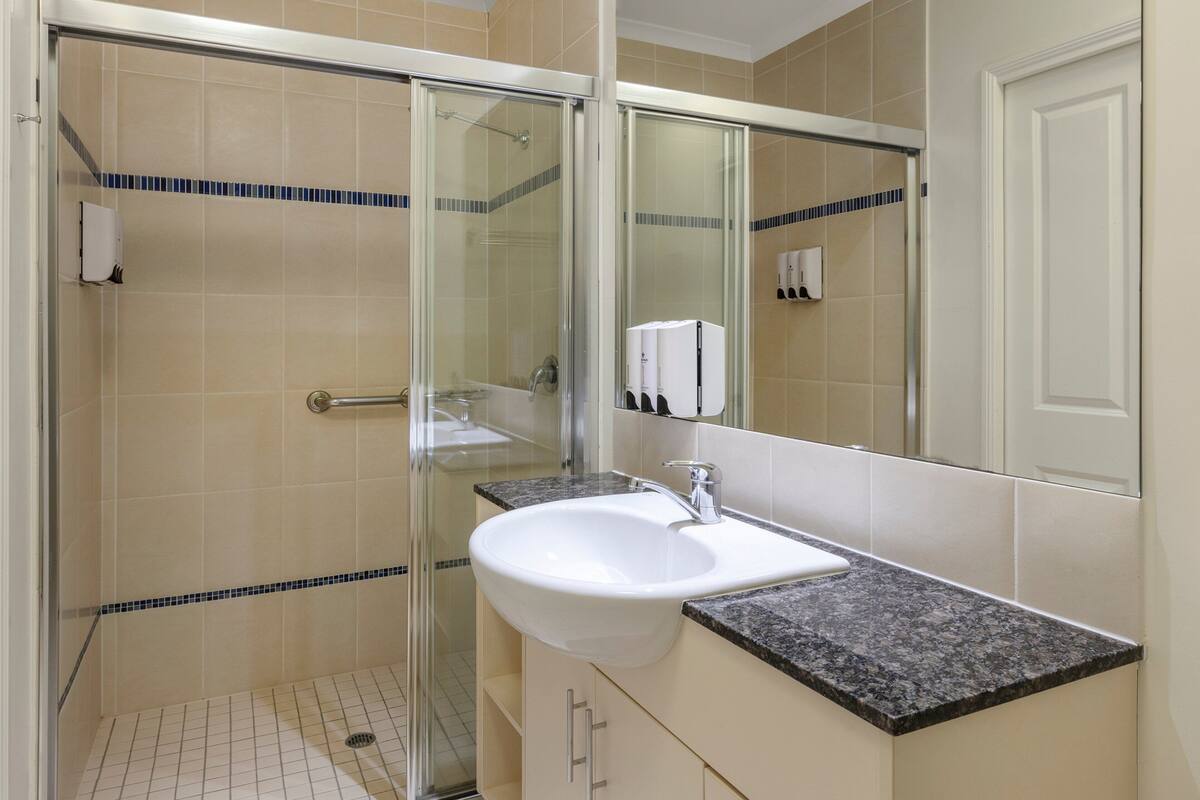 A modern bathroom with a glass-enclosed shower, a white sink, and a large mirror.
