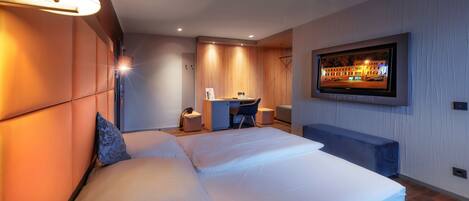 A modern hotel room with a large bed, a desk, and a television on the wall.