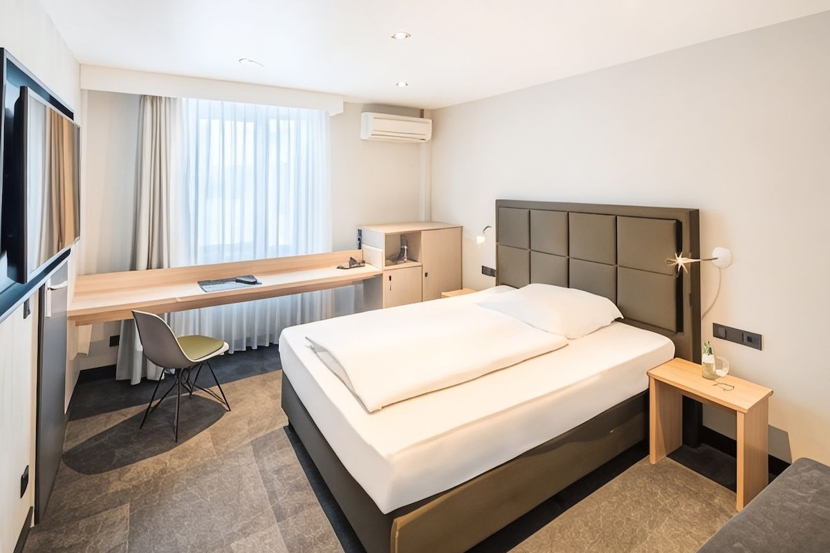 A hotel room with a bed, desk, chair, and a TV.