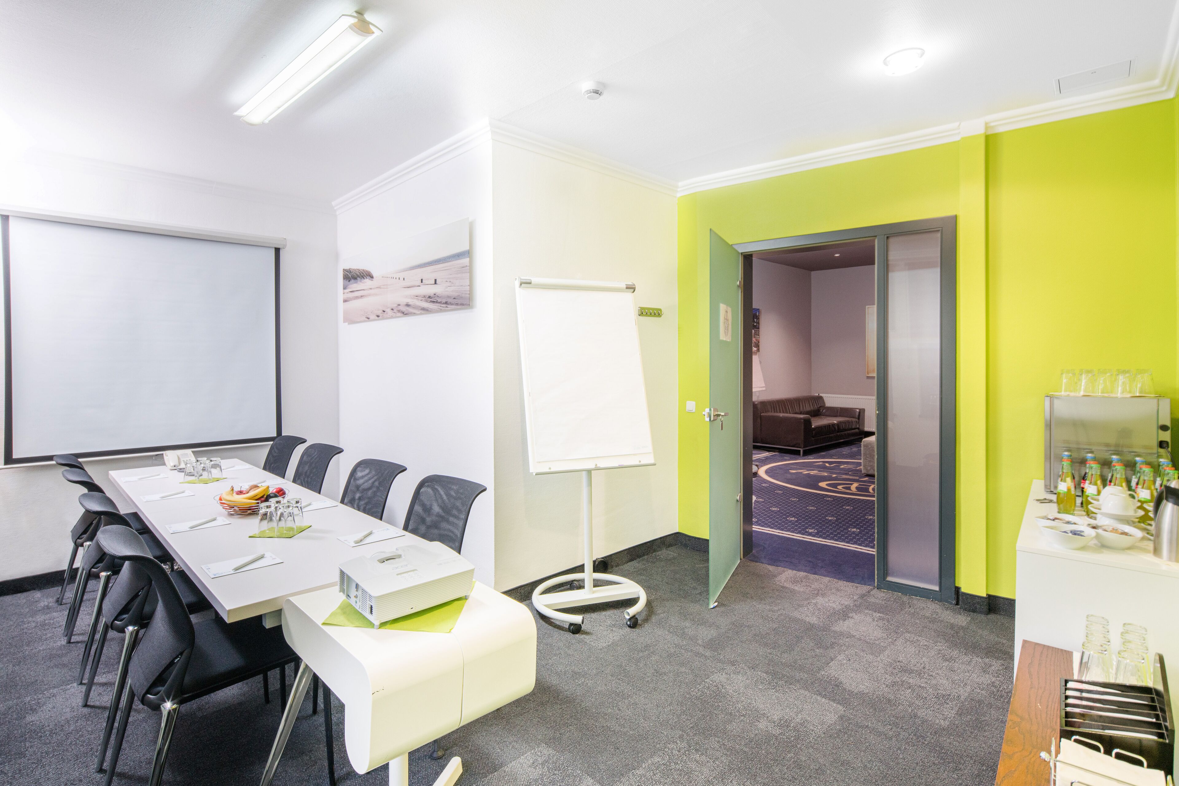 Een vergaderzaal met een lange tafel, stoelen, een whiteboard en een projectiescherm.