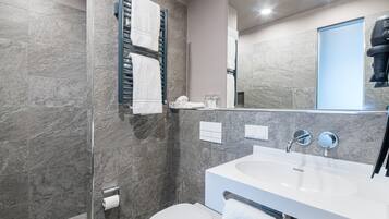 Ein modernes Badezimmer mit Duschkabine aus Glas, Toilette in Weiß, großem Waschbecken mit Spiegel und Handtuchhalter.