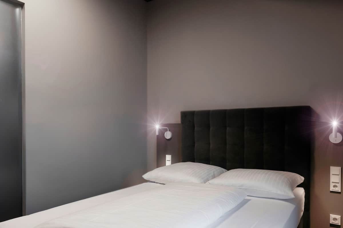 A modern bedroom with a large bed, a dark headboard, and two wall-mounted lights.