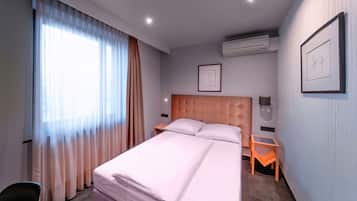 Quarto de hotel com uma cama grande, mesa de cabeceira, uma cadeira e um quadro na parede.