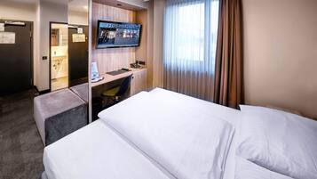 A hotel room with a bed, a desk with a computer, a TV, and a window with curtains.