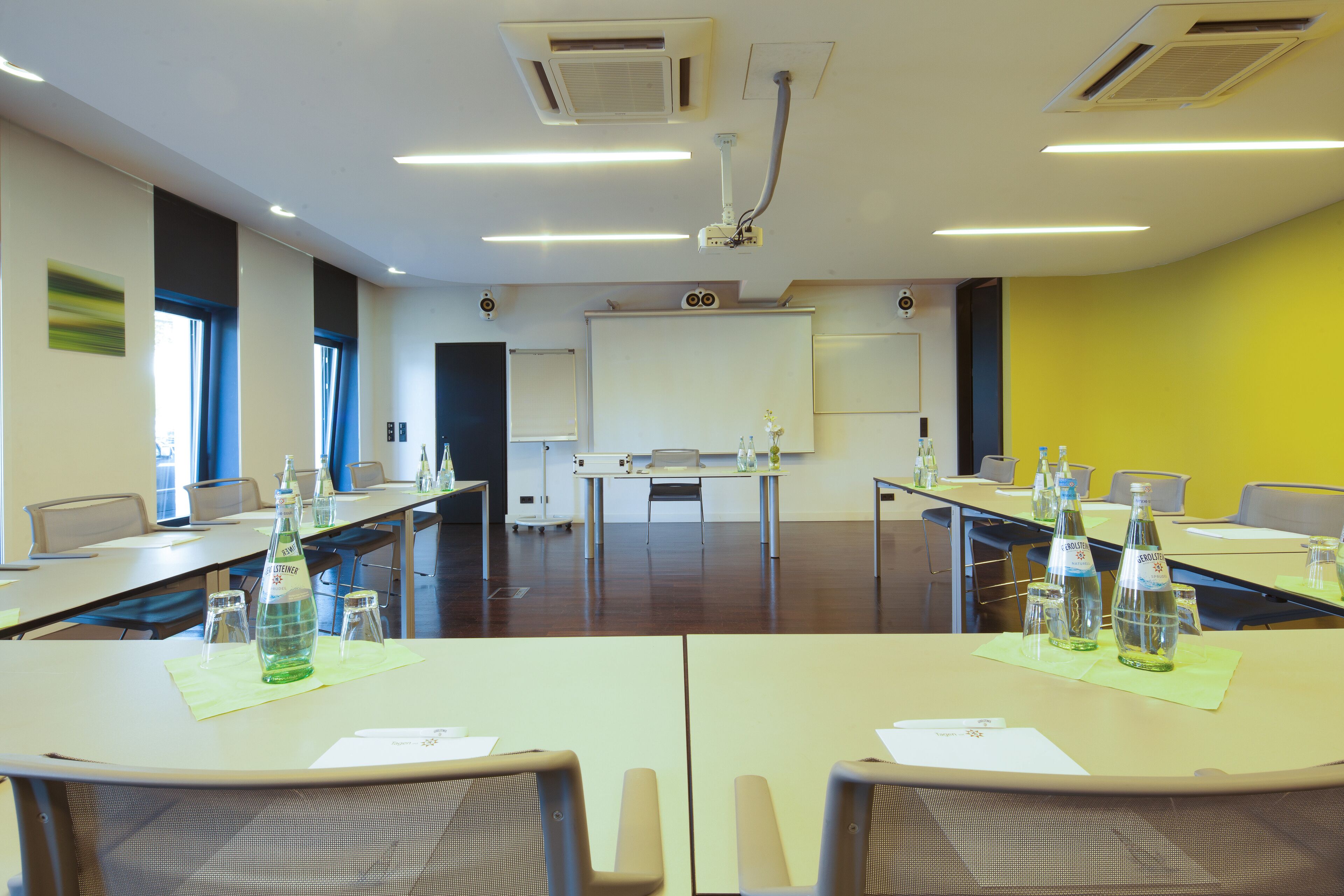 Ein Konferenzraum mit einer Whiteboard, einem Projektor und Tischen mit Wasserflaschen.