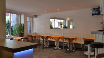 Ein Restaurant mit orangefarben gedeckten Tischen, einem Blumentopf und einem an der Wand befestigten Fernseher.
